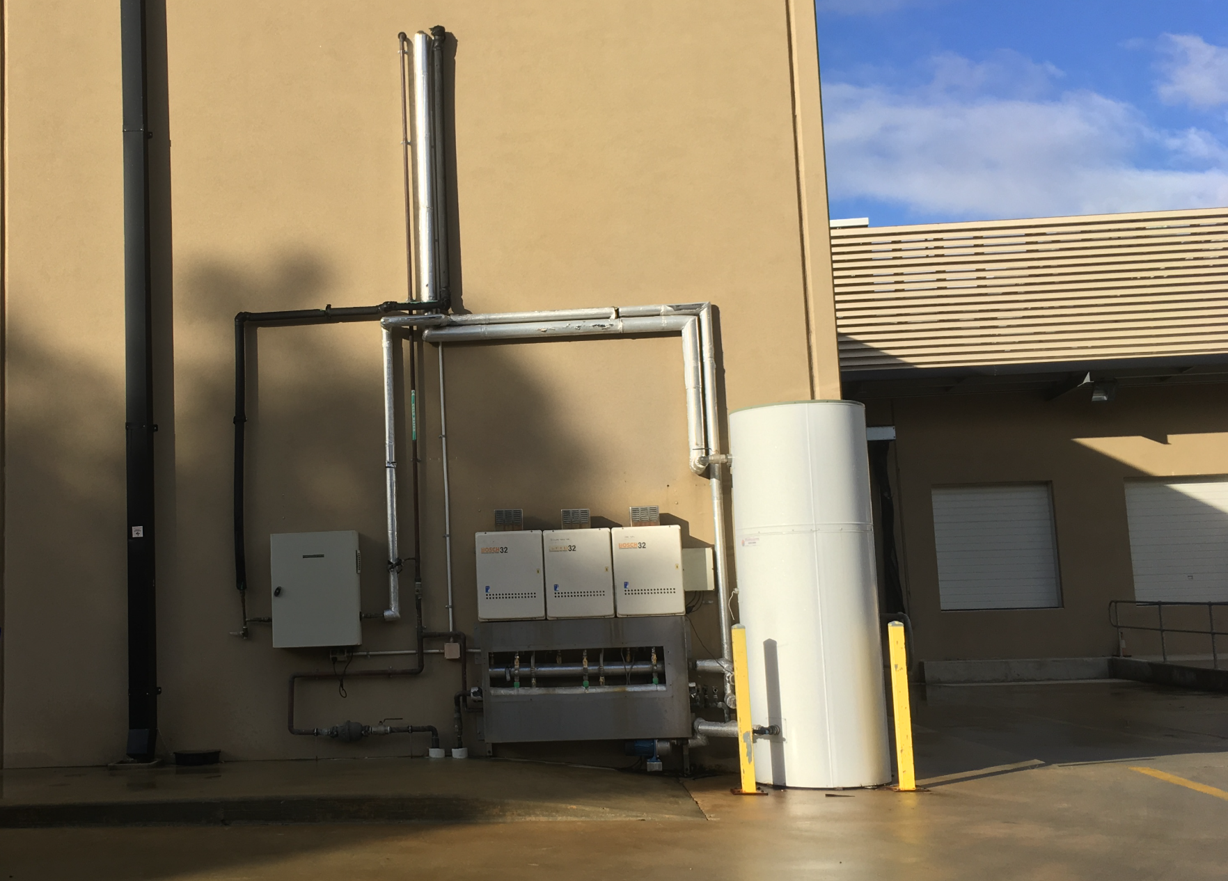 External commercial hot water plant — three gas continuous-flow heaters, flue and a storage cylinder.